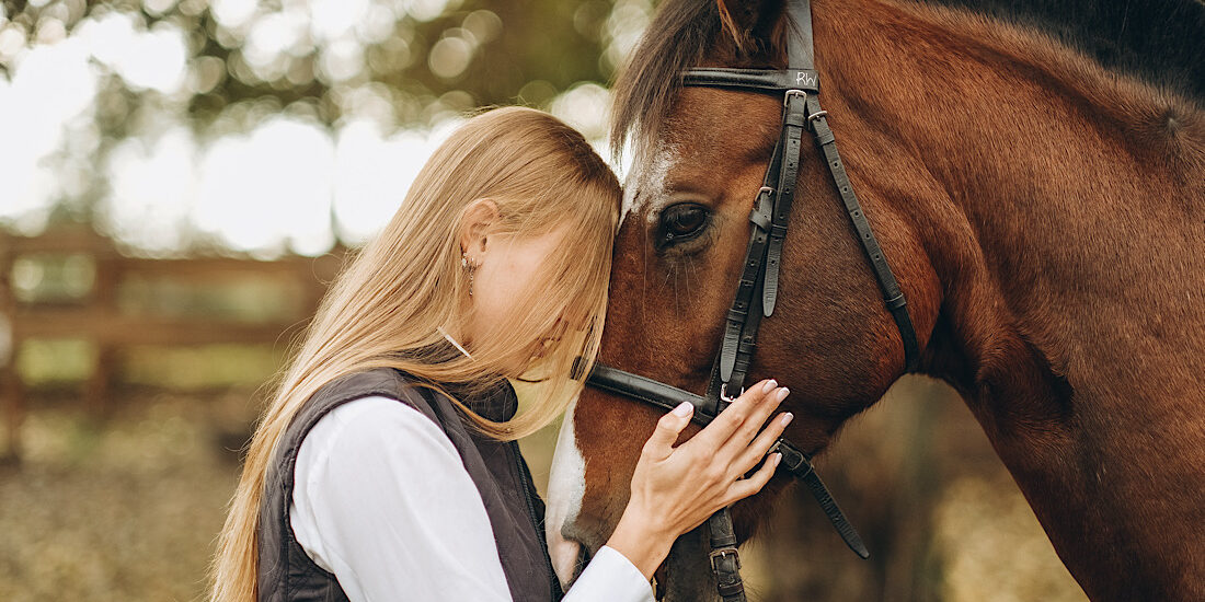 A young female equestrian stands near her horse and prepares for a competition. Show jumping training. Love for horses.