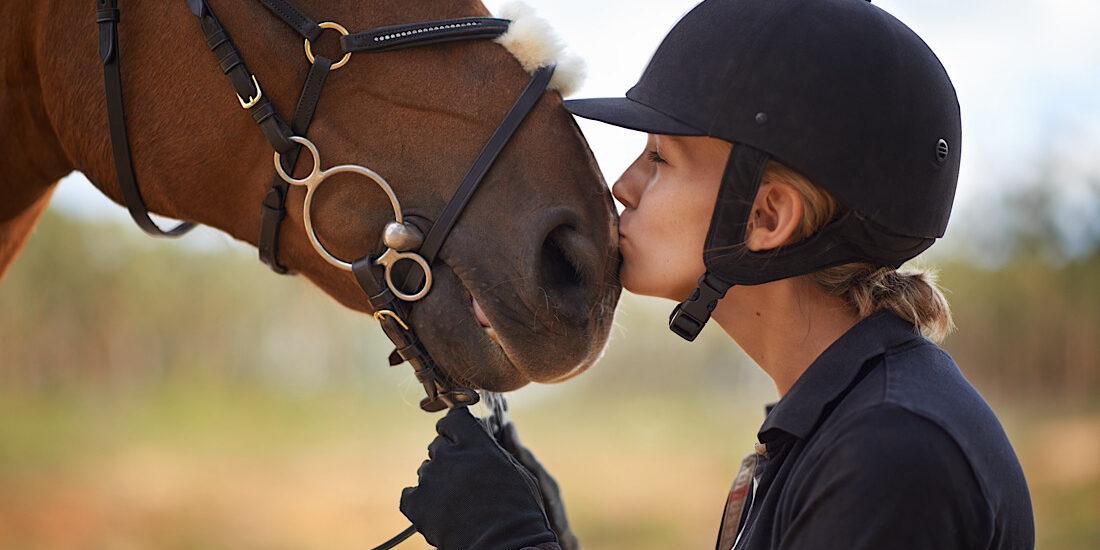 A young female rider being affectionate with her chestnut horse